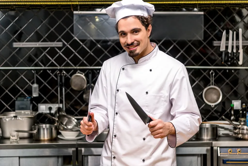 https://www.chefsdeal.com/blog/wp-content/uploads/2023/05/smiling-chef-with-comemrcial-kitchen-knives-jpg.webp